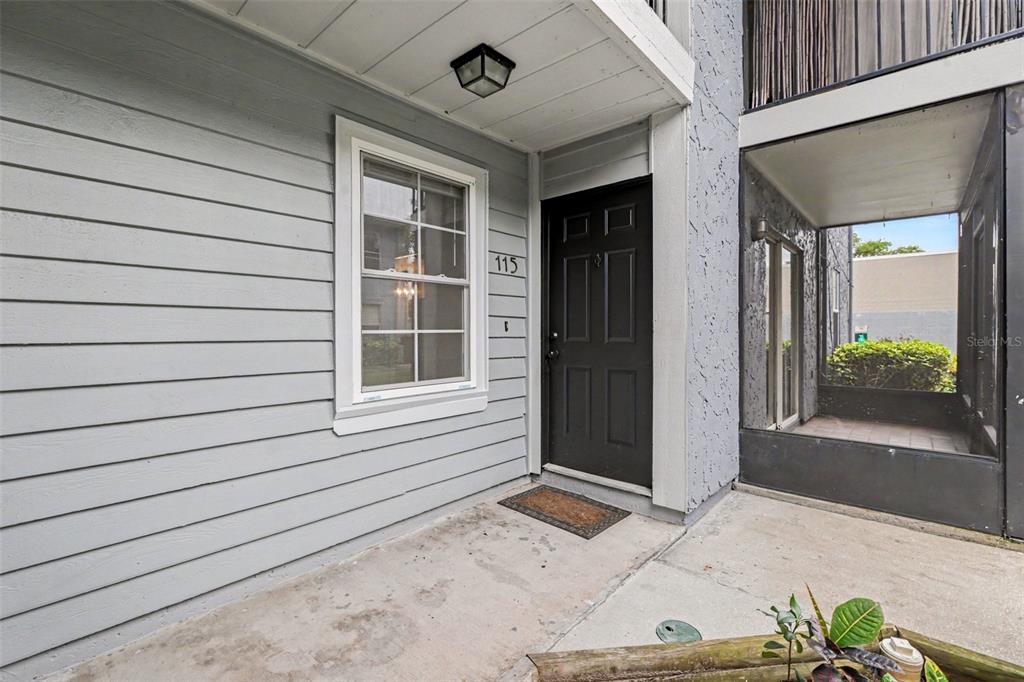 The exterior view shows a gray-sided building entrance with a black door and concrete porch — 3711 W IOWA AVE UNIT 115, TAMPA, FL