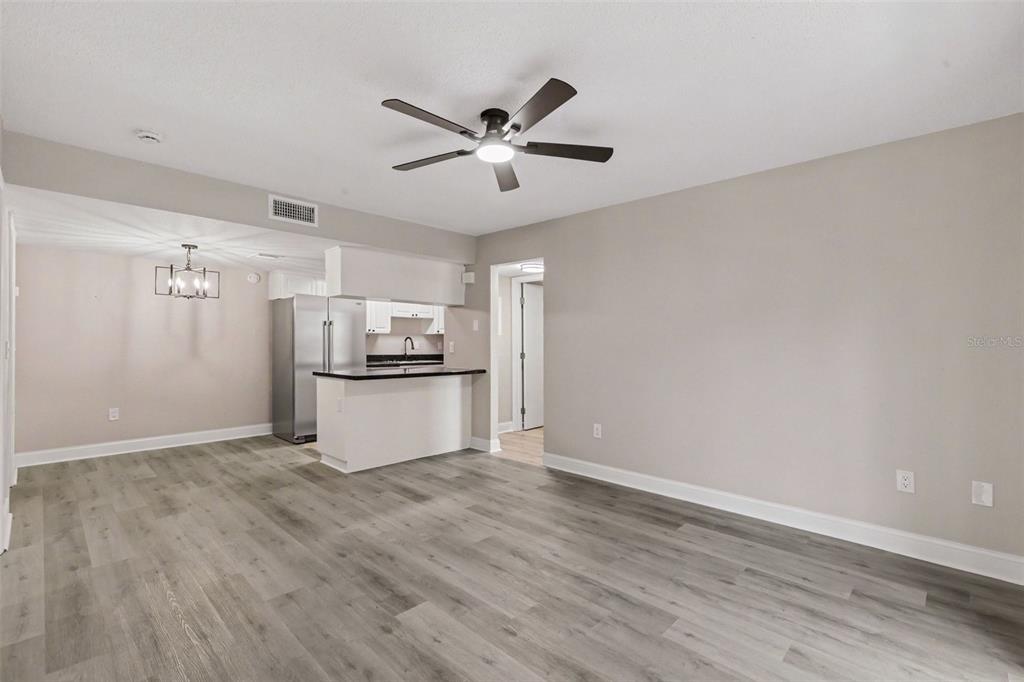 A living room with gray wood-look flooring, a ceiling fan, and an open kitchen area — 3711 W IOWA AVE UNIT 115, TAMPA, FL