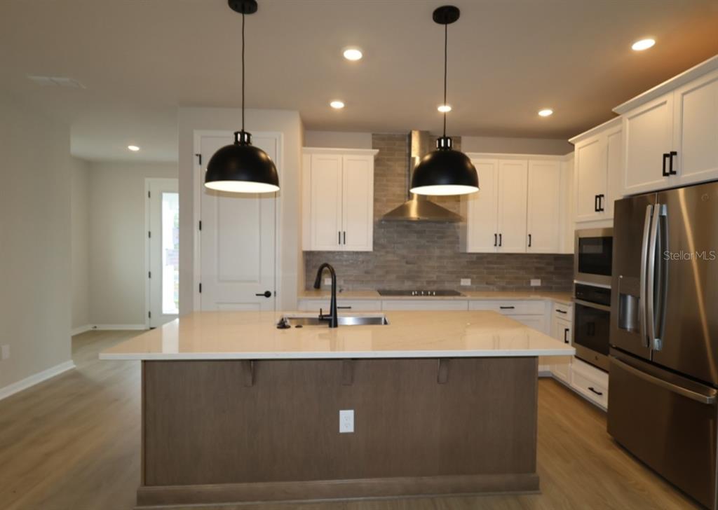 A kitchen features a central island, white cabinetry, stainless steel appliances, and two pendant lights — 6716 FOUNTAIN GROVE PASS, ST CLOUD, FL