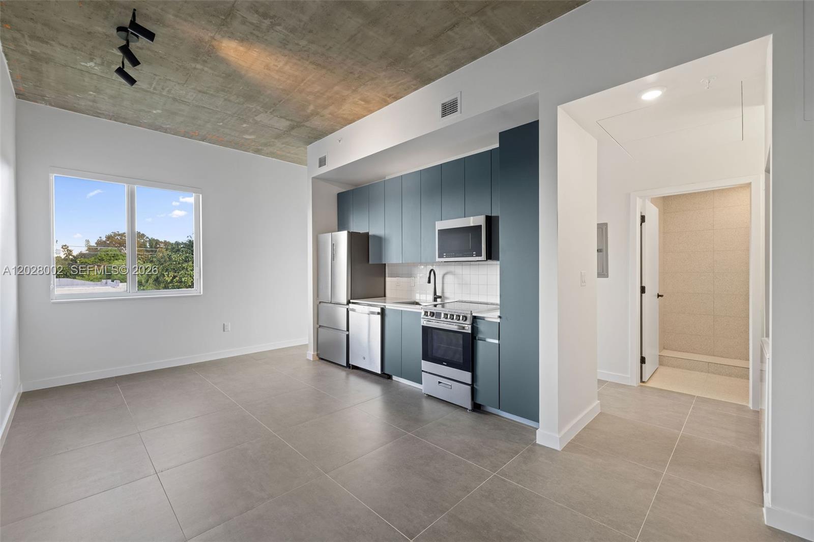 A modern kitchen with blue cabinetry and stainless steel appliances sits beneath a concrete ceiling — 315 NW 32 ST # 306, Miami FL 33127, MIAMI, FL