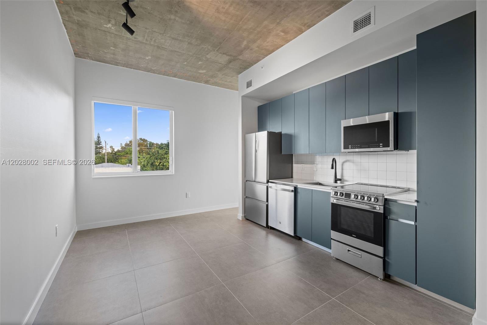 A modern kitchen features blue cabinets, stainless steel appliances, and a raw concrete ceiling — 315 NW 32 ST # 306, Miami FL 33127, MIAMI, FL