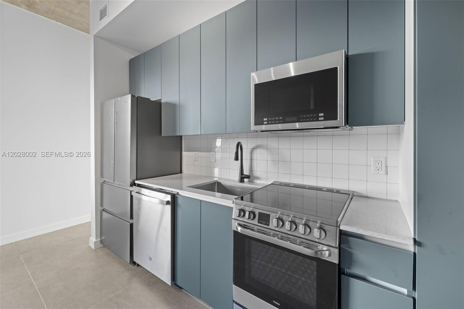 A modern kitchen features blue cabinets, stainless steel appliances, and white tiled backsplashes — 315 NW 32 ST # 306, Miami FL 33127, MIAMI, FL