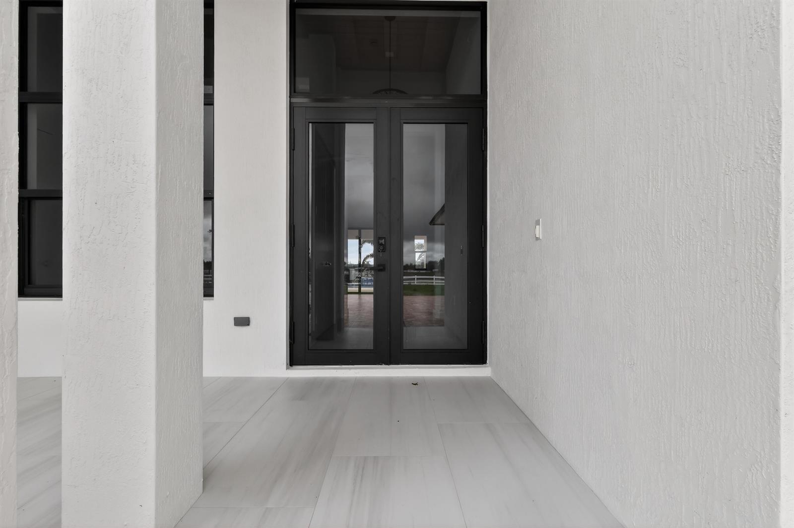 A covered entryway features white stucco walls, light tile flooring, and black-framed glass double doors — 3644 Frog Holw, Loxahatchee FL 33470, LOXAHATCHEE, FL