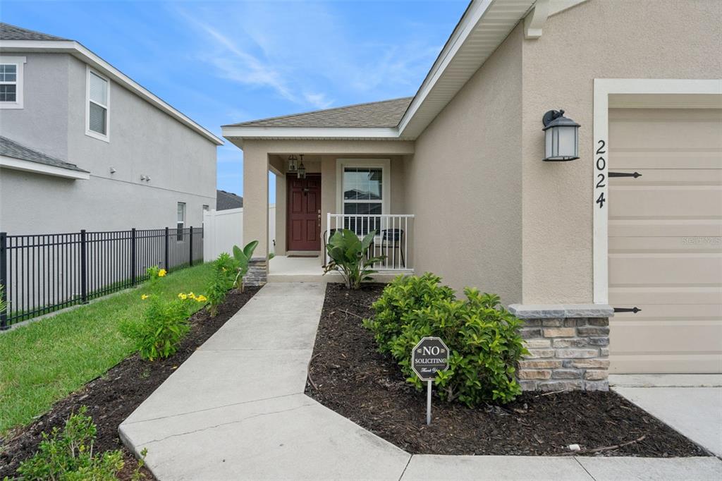 A concrete walkway leads to the front entrance of a house with beige stucco siding — 2024 NOBLE DRIVE, DAVENPORT, FL