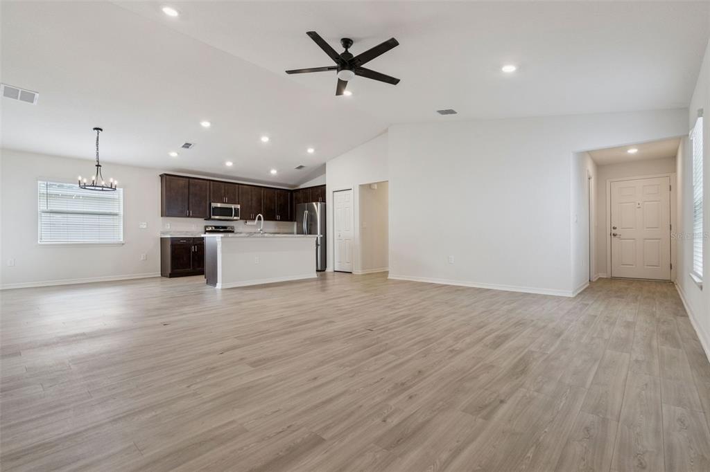 An open-concept living area features light wood-look flooring, a kitchen with dark cabinets, and white walls — 2024 NOBLE DRIVE, DAVENPORT, FL