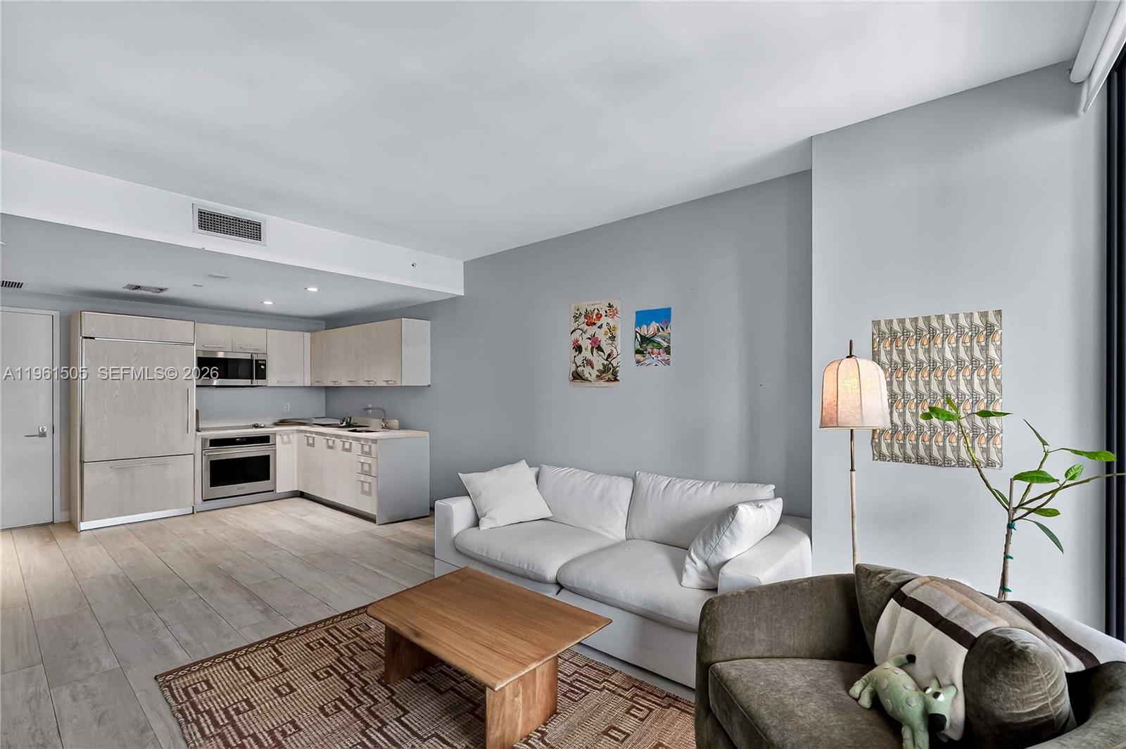 A modern open-concept living room features a white sofa, wooden coffee table, and adjacent kitchen — 45 SW 9th St # 3807, Miami FL 33130, MIAMI, FL