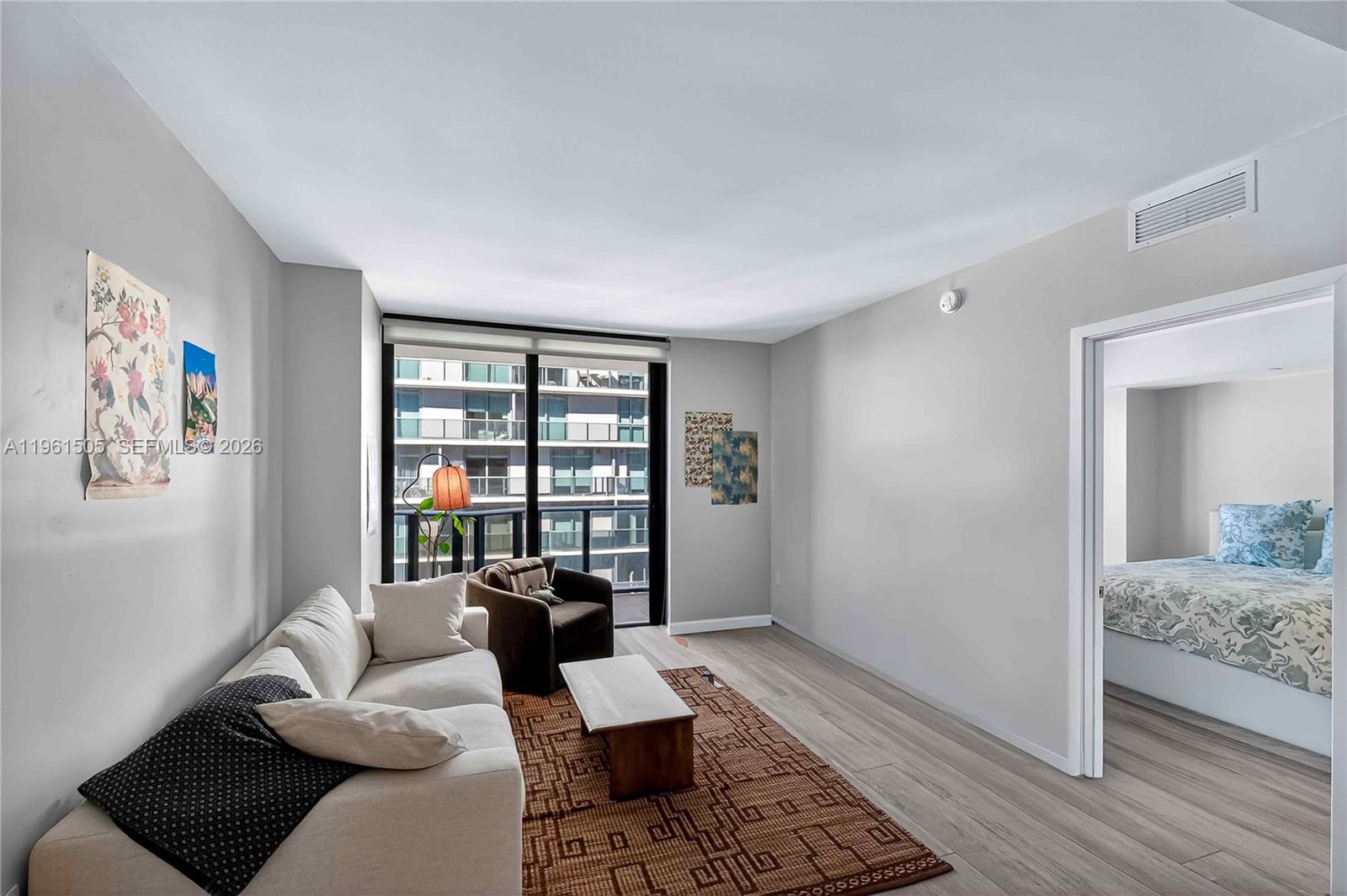 A living room features light wood-look flooring, a beige sofa, and a view of buildings — 45 SW 9th St # 3807, Miami FL 33130, MIAMI, FL