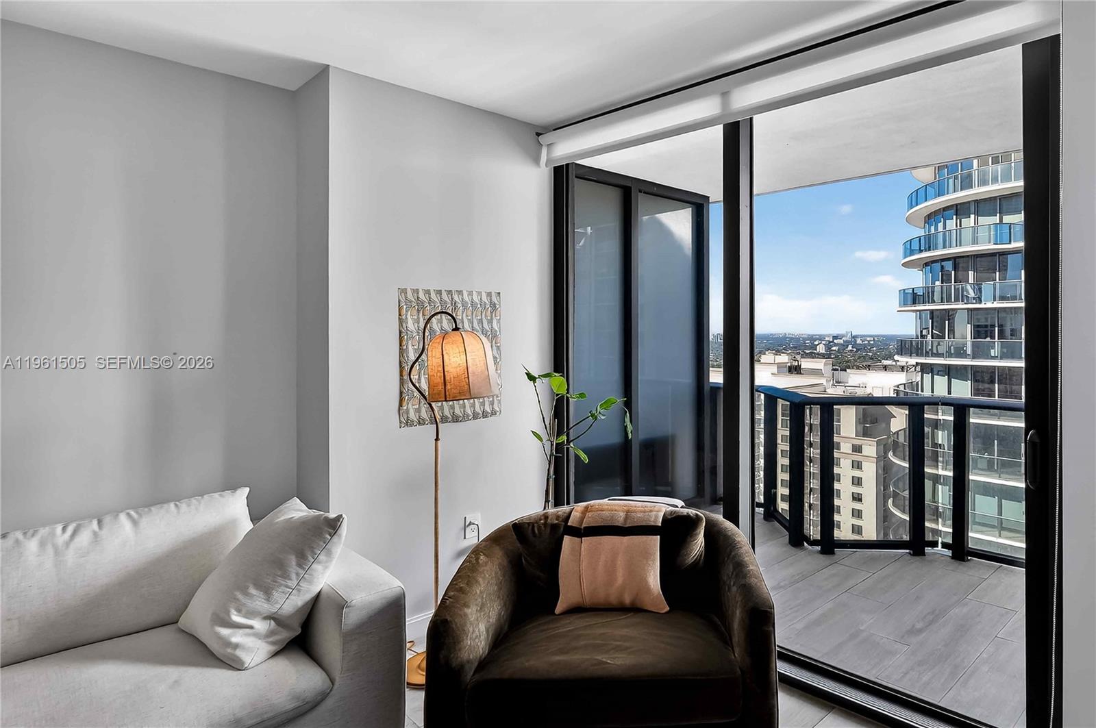 A living room features a dark armchair, a floor lamp, and a balcony with city views — 45 SW 9th St # 3807, Miami FL 33130, MIAMI, FL