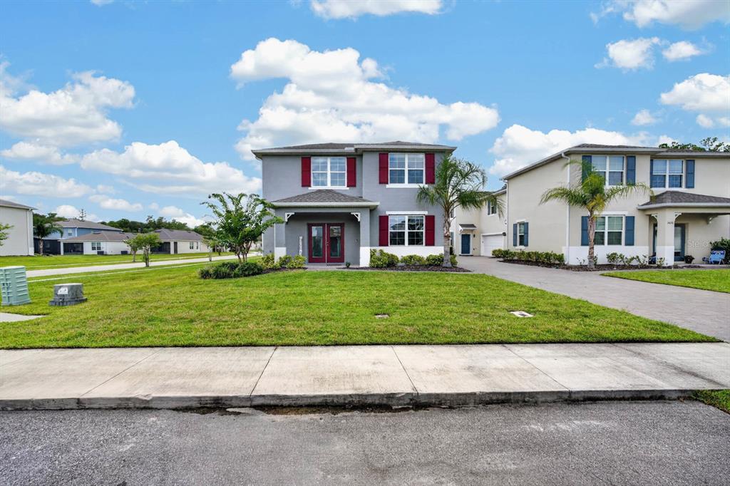 A two-story gray house with red shutters and a front lawn under a blue sky — 3006 MELETO BOULEVARD, NEW SMYRNA BEACH, FL