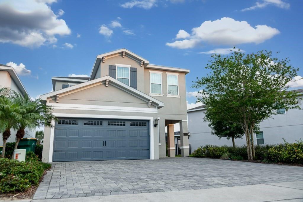 A two-story house with a gray garage door and a paved driveway under a blue sky — 7420 MARKER AVENUE, KISSIMMEE, FL