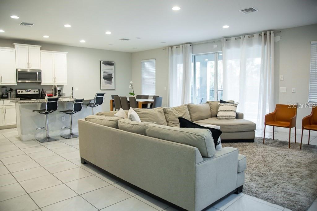 An open-concept living room and kitchen featuring a large sectional sofa and white cabinetry — 7420 MARKER AVENUE, KISSIMMEE, FL