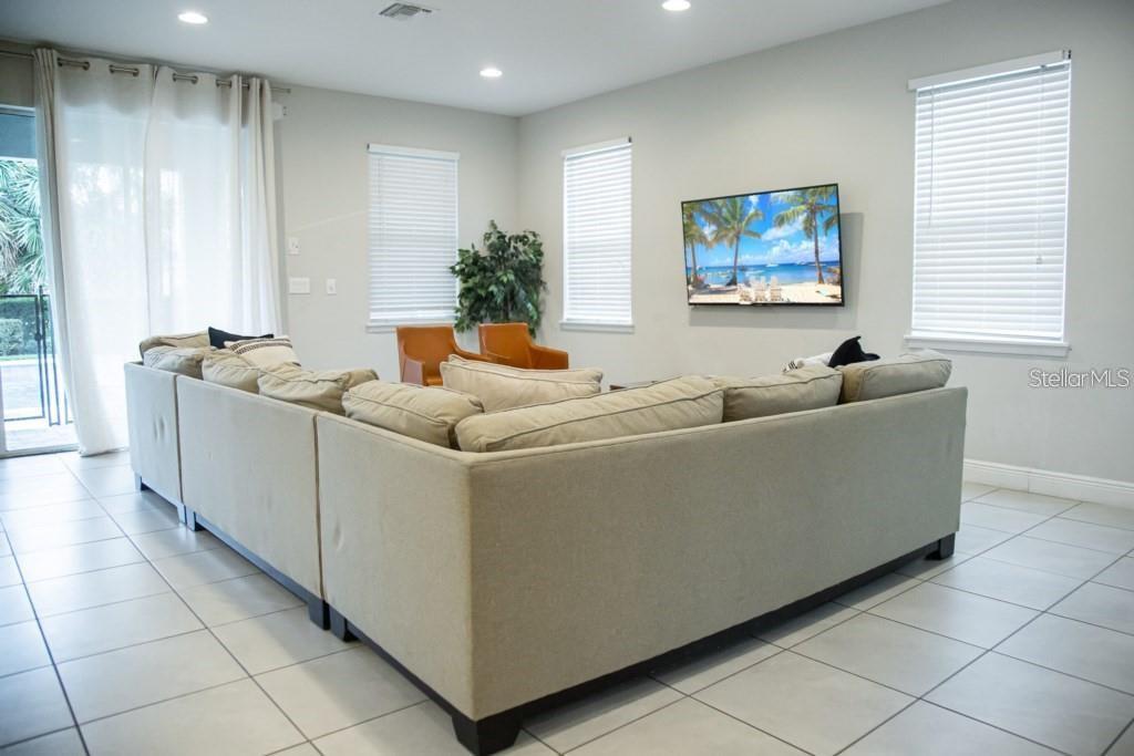 A living room features a large beige sectional sofa, two orange chairs, and a wall-mounted television — 7420 MARKER AVENUE, KISSIMMEE, FL