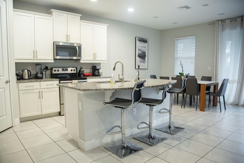 A kitchen features white cabinets, granite countertops, a center island with bar stools, and tile flooring — 7420 MARKER AVENUE, KISSIMMEE, FL