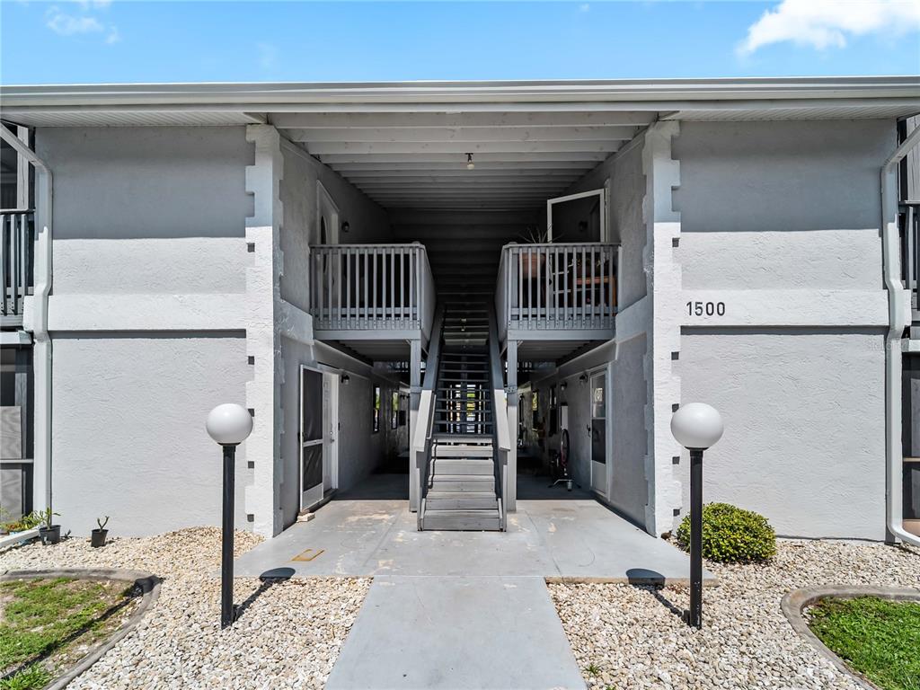 A two-story apartment building exterior features a central staircase leading to upper-level balconies — 22441 WESTCHESTER BOULEVARD UNIT 1500F, PUNTA GORDA, FL