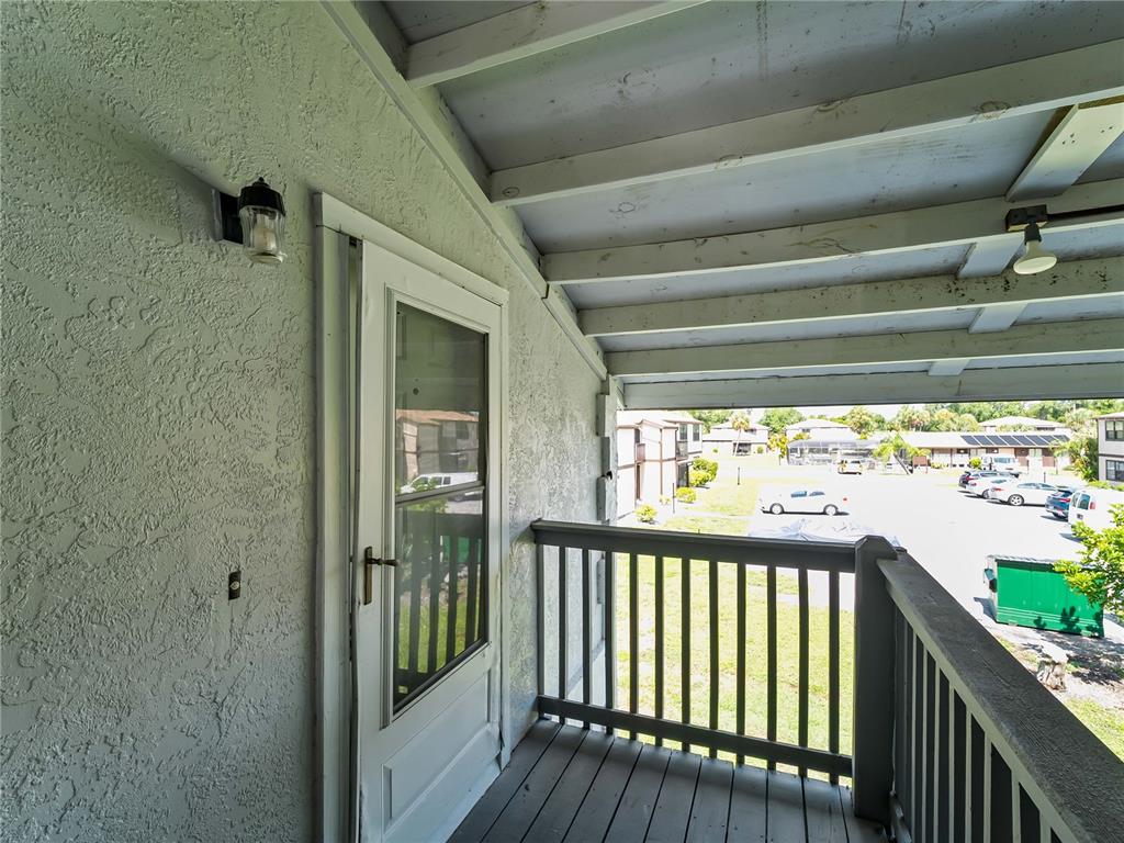 A covered balcony with a white storm door, wooden railing, and a view of parking — 22441 WESTCHESTER BOULEVARD UNIT 1500F, PUNTA GORDA, FL
