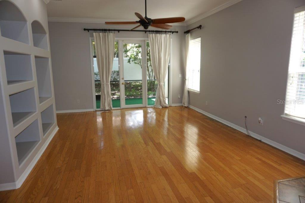 A living room with hardwood floors, built-in shelving, a ceiling fan, and glass patio doors — 8406 FRESCADA COURT, ORLANDO, FL