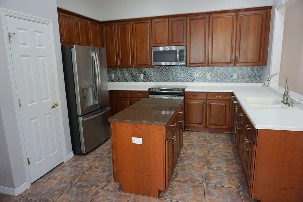 A kitchen features wood cabinets, stainless steel appliances, a center island, and a mosaic backsplash — 8406 FRESCADA COURT, ORLANDO, FL