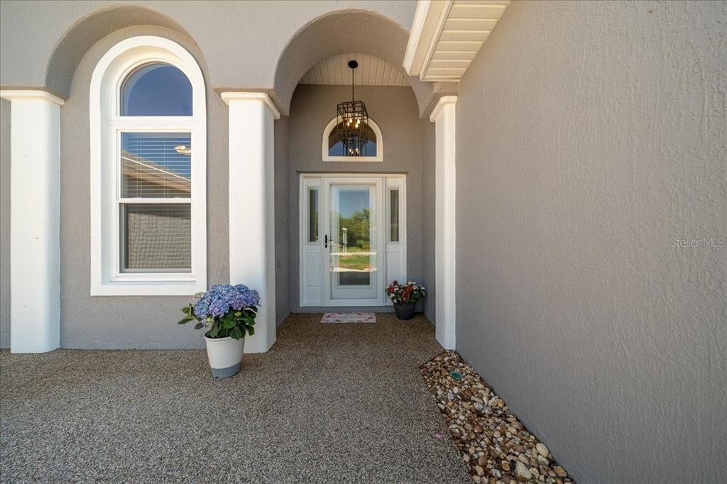 A gray house exterior features a covered entryway with white columns and a glass door — 6790 SW 117TH STREET, OCALA, FL