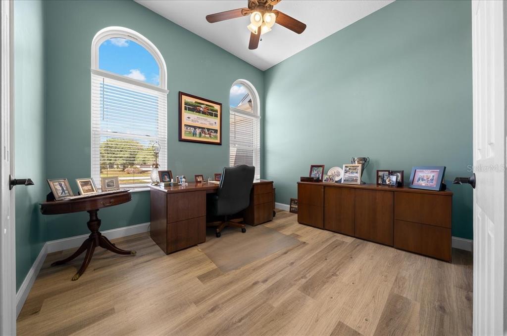 A home office features light wood flooring, teal walls, two arched windows, and wooden furniture — 6790 SW 117TH STREET, OCALA, FL