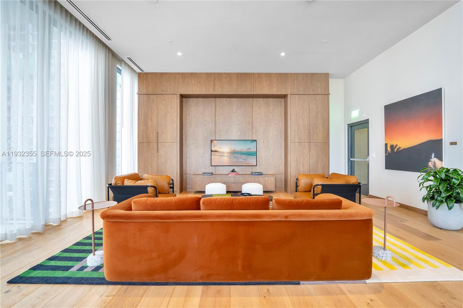 A modern living room features a large orange sofa, wood wall paneling, and a television — 11 NE 6 Street # 2201, Miami FL 33132, MIAMI, FL