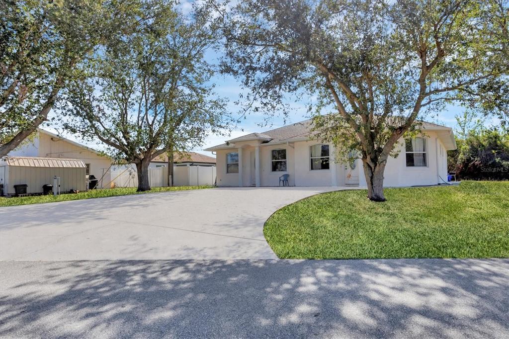 A single-story house with a concrete driveway, large trees, and a detached storage shed — 12113 CAPILLA LANE, NORTH PORT, FL