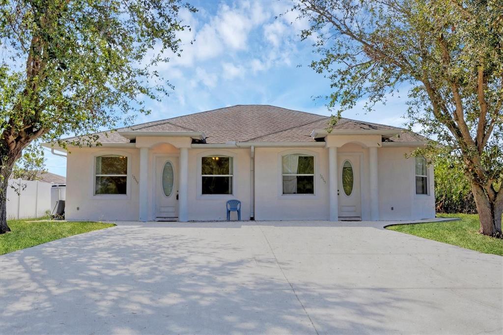 A single-story duplex with a concrete driveway, two front entrances, and two large trees — 12113 CAPILLA LANE, NORTH PORT, FL