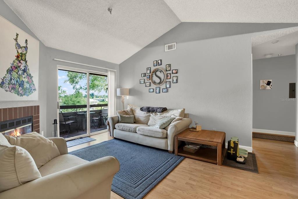 A living room features a vaulted ceiling, a fireplace, a sofa, and a sliding glass door — 10265 GANDY BOULEVARD N UNIT 906, ST PETERSBURG, FL