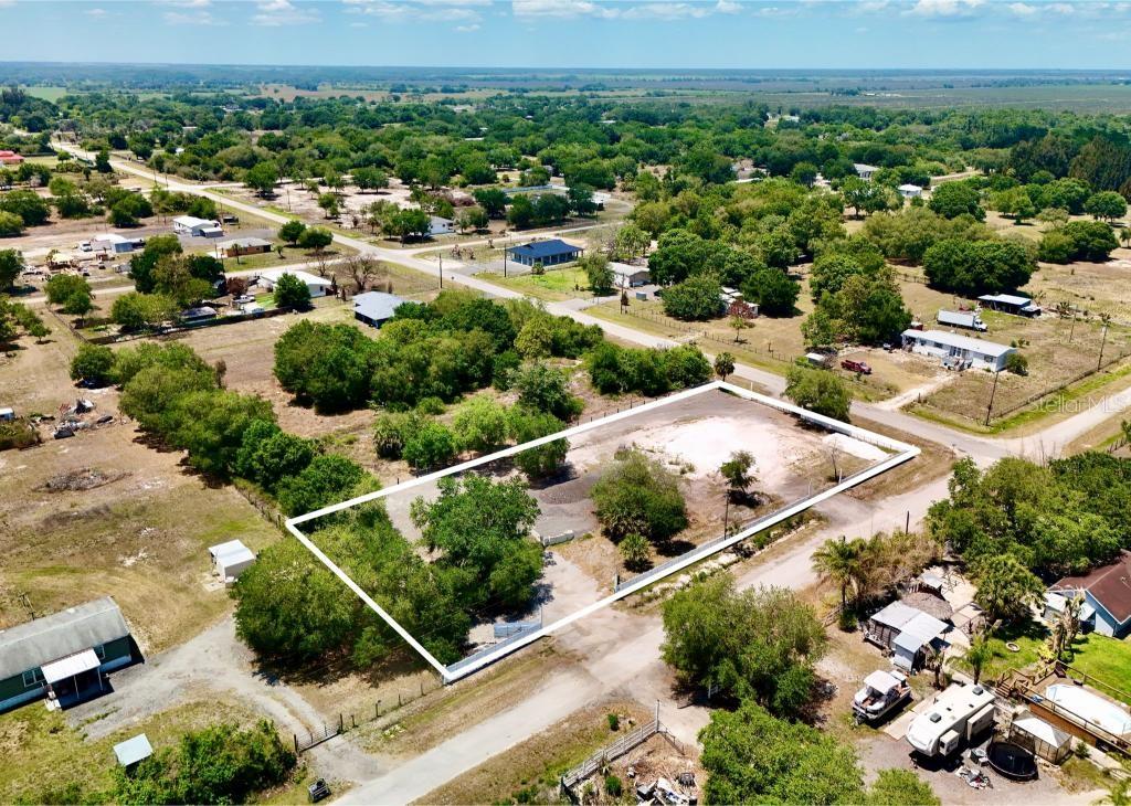 An aerial view shows a fenced, rectangular vacant lot with trees and a gravel area — 242 BALD CYPRESS AVENUE, CLEWISTON, FL