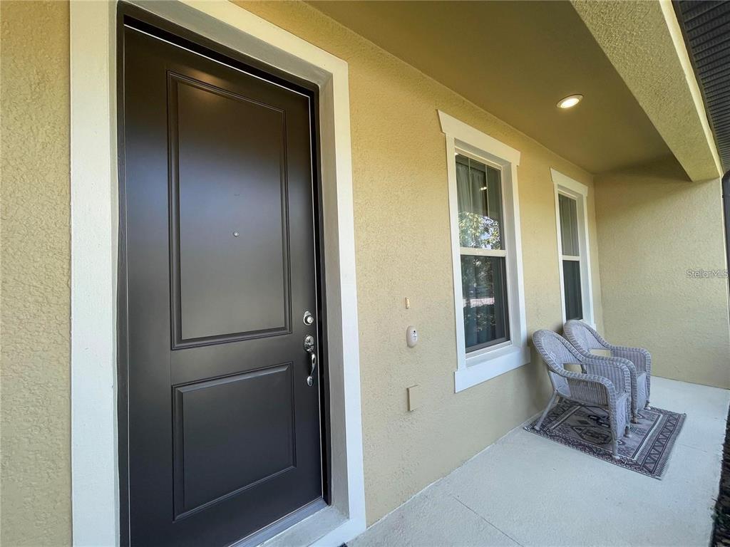 A dark front door and two wicker chairs sit on a covered concrete porch — 5032 WALKER STREET, ST CLOUD, FL