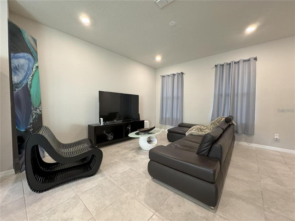 A living room features light tile flooring, a black leather sofa, and a modern accent chair — 5032 WALKER STREET, ST CLOUD, FL