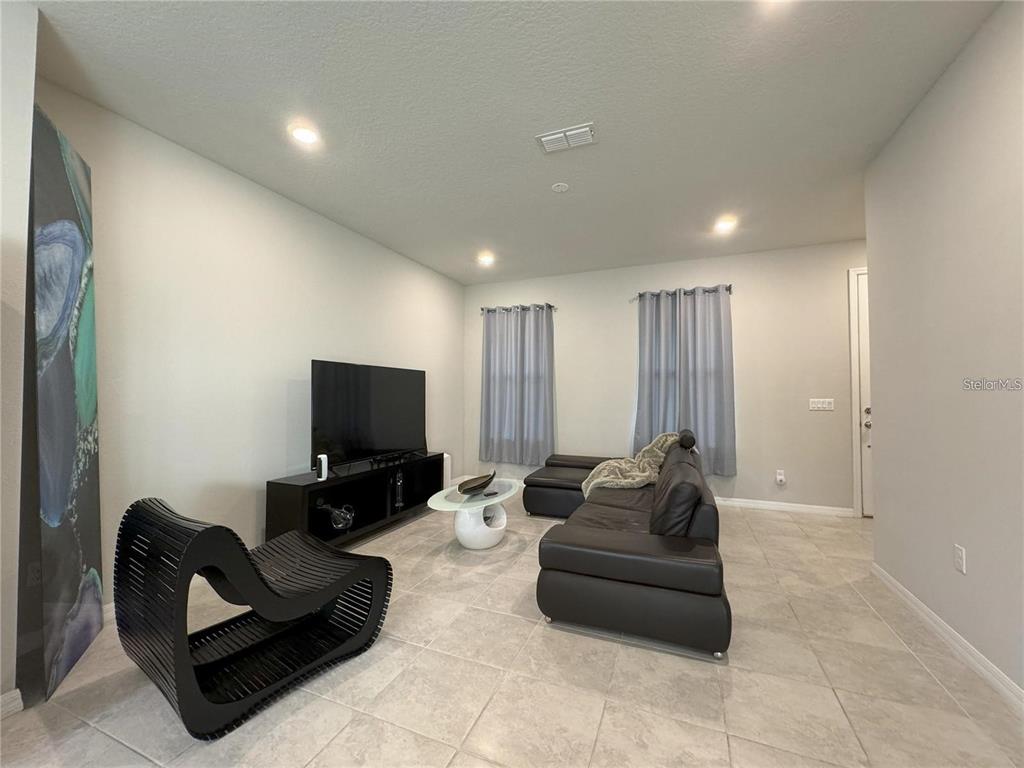 A living room features light tile flooring, a black leather sofa, and a modern accent chair — 5032 WALKER STREET, ST CLOUD, FL