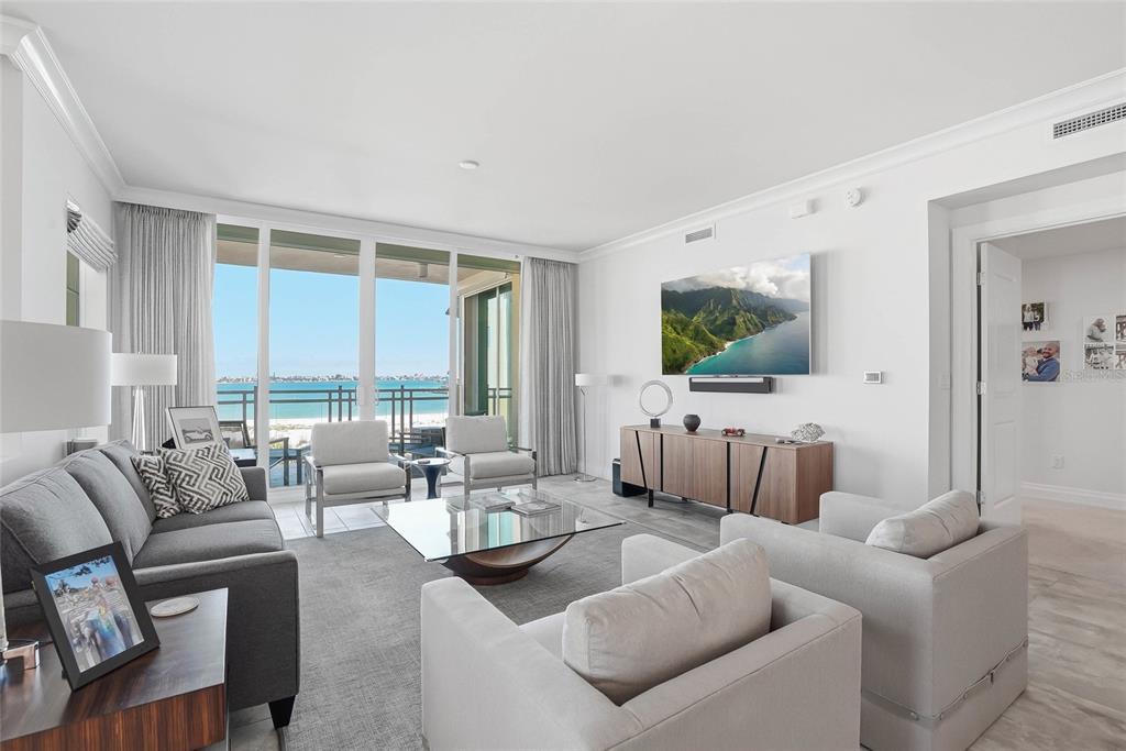 A bright living room features a gray sofa, two armchairs, a glass coffee table, and ocean views — 650 COLLANY ROAD UNIT 401, TIERRA VERDE, FL