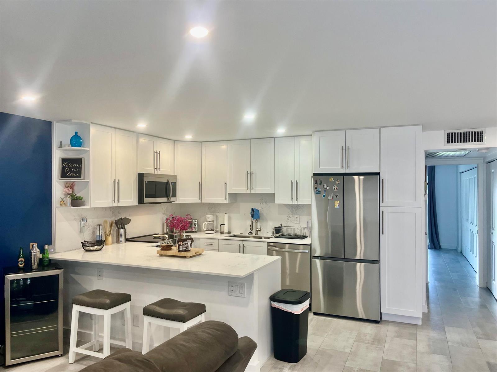 A modern kitchen features white cabinets, stainless steel appliances, a breakfast bar, and tile flooring — 2036 Harwood D, Deerfield Beach FL 33442, DEERFIELD BEACH, FL