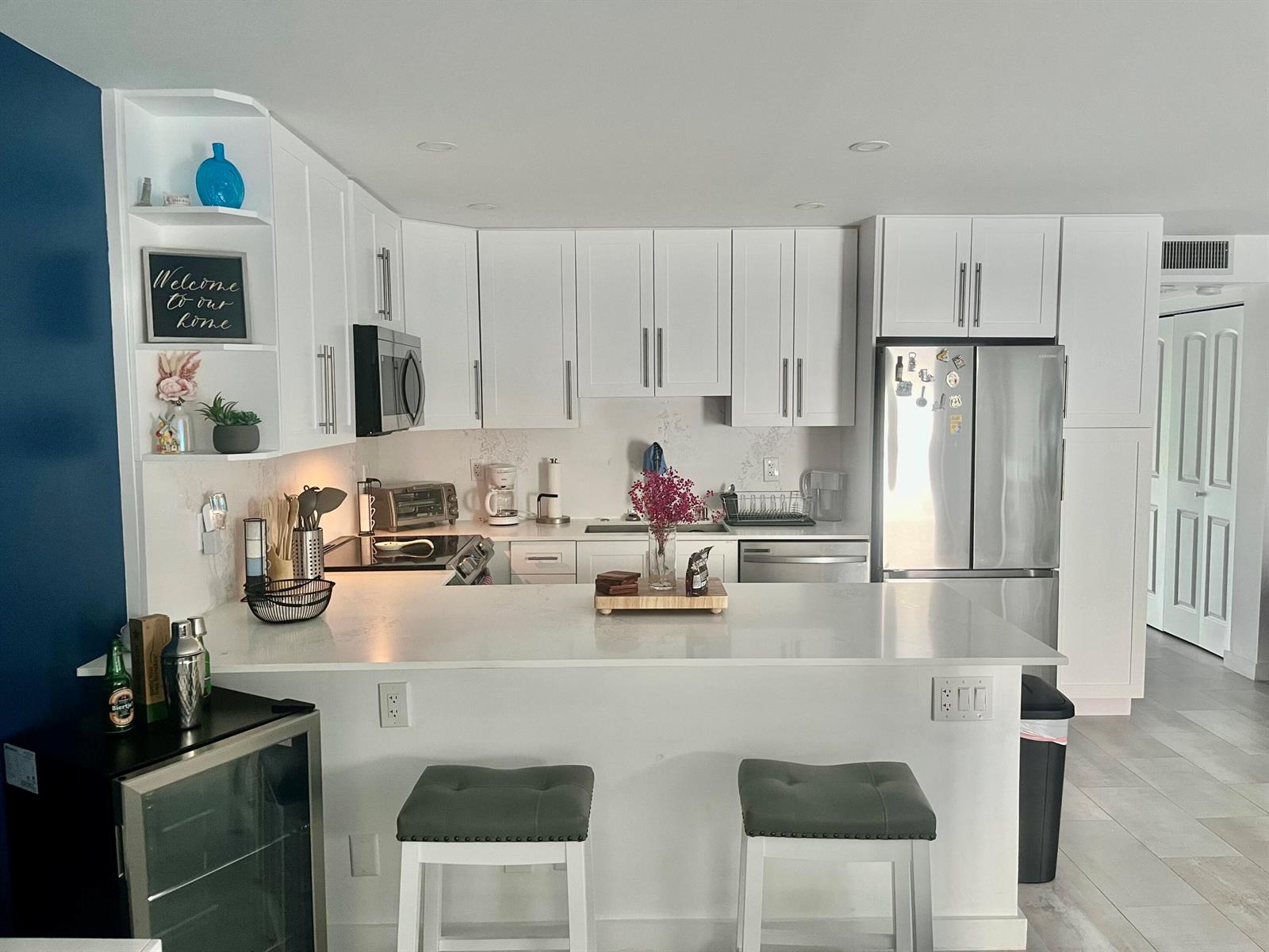 A modern kitchen features white cabinets, stainless steel appliances, a quartz countertop, and two barstools — 2036 Harwood D, Deerfield Beach FL 33442, DEERFIELD BEACH, FL
