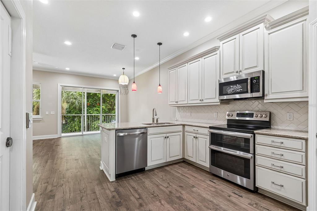 A kitchen with white cabinets, stainless steel appliances, and wood-look flooring opens to a balcony — 3144 NAUTICAL PLACE S, ST PETERSBURG, FL