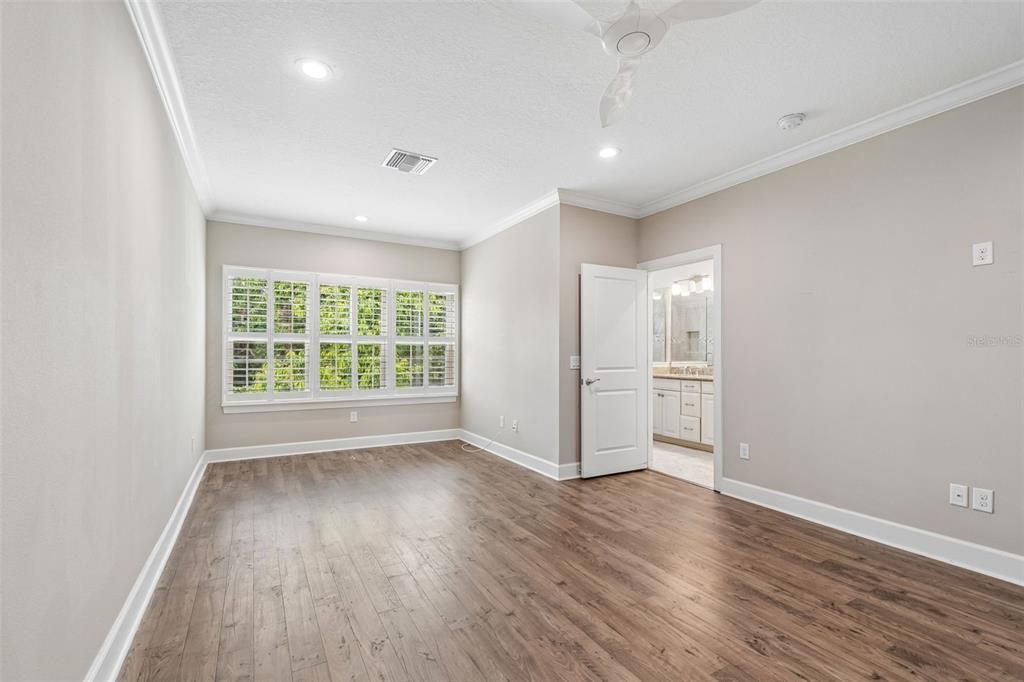 An empty bedroom features wood-look flooring, white plantation shutters, and an attached bathroom — 3144 NAUTICAL PLACE S, ST PETERSBURG, FL