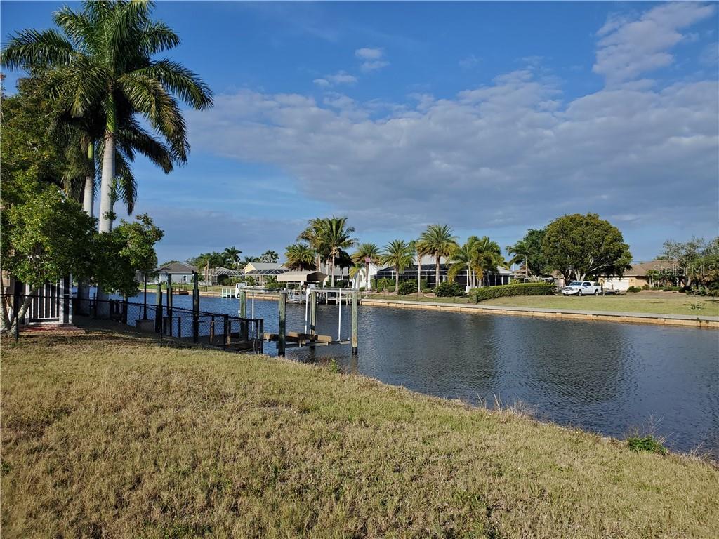 A canal view from a grassy backyard featuring a boat dock and palm trees — 4228 EASTLAKE COURT, PORT CHARLOTTE, FL