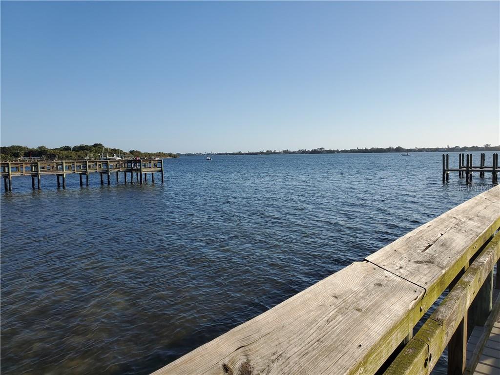 A wooden pier extends into a calm bay under a clear blue sky — 4228 EASTLAKE COURT, PORT CHARLOTTE, FL