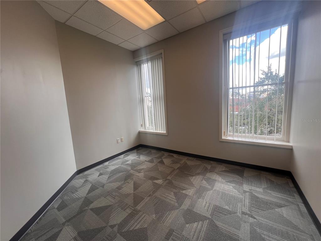 An empty office with gray patterned carpet, beige walls, and two windows with vertical blinds — 110 W 1ST STREEET UNIT 210, SANFORD, FL