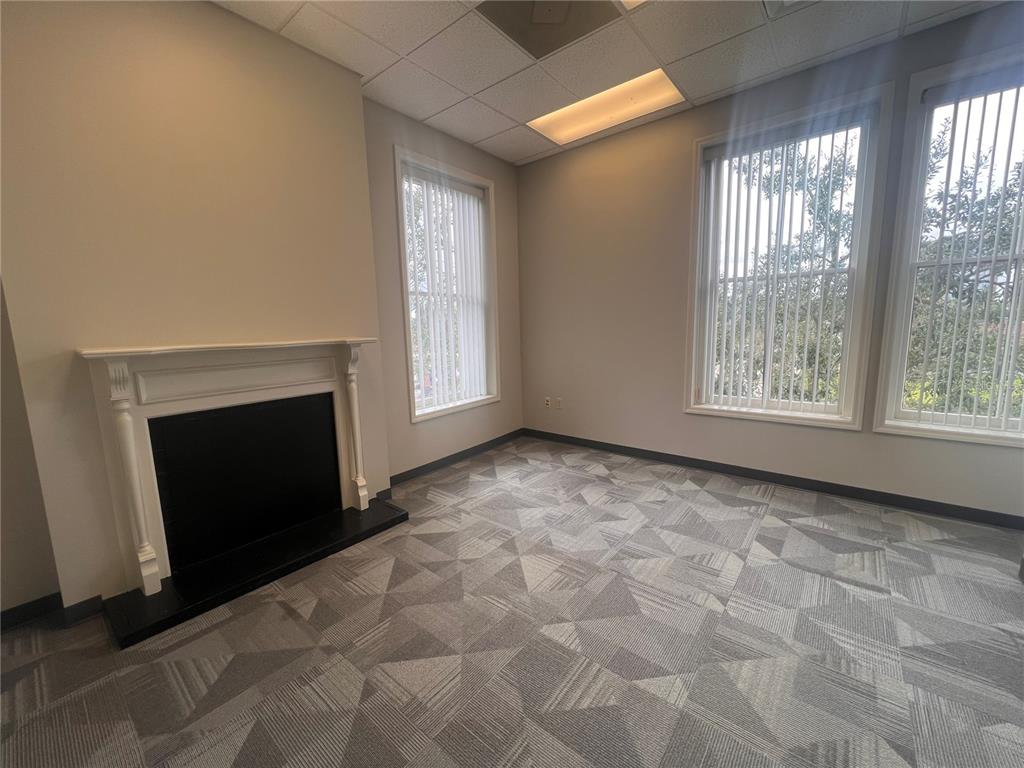 An office room features a fireplace, gray patterned carpet, and large windows with vertical blinds — 110 W 1ST STREEET UNIT 210, SANFORD, FL