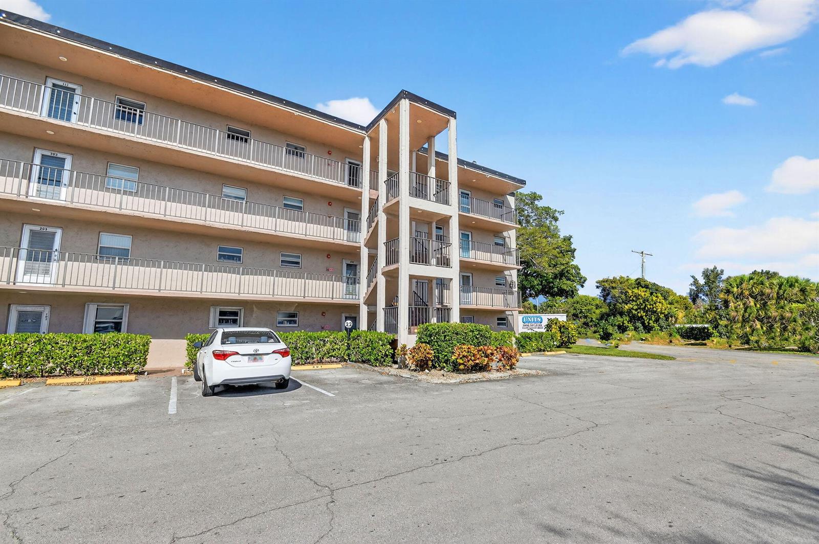 A three-story apartment building features exterior balconies and a parking lot in the foreground — 729 Lori Drive # 302, Palm Springs FL 33461, PALM SPRINGS, FL