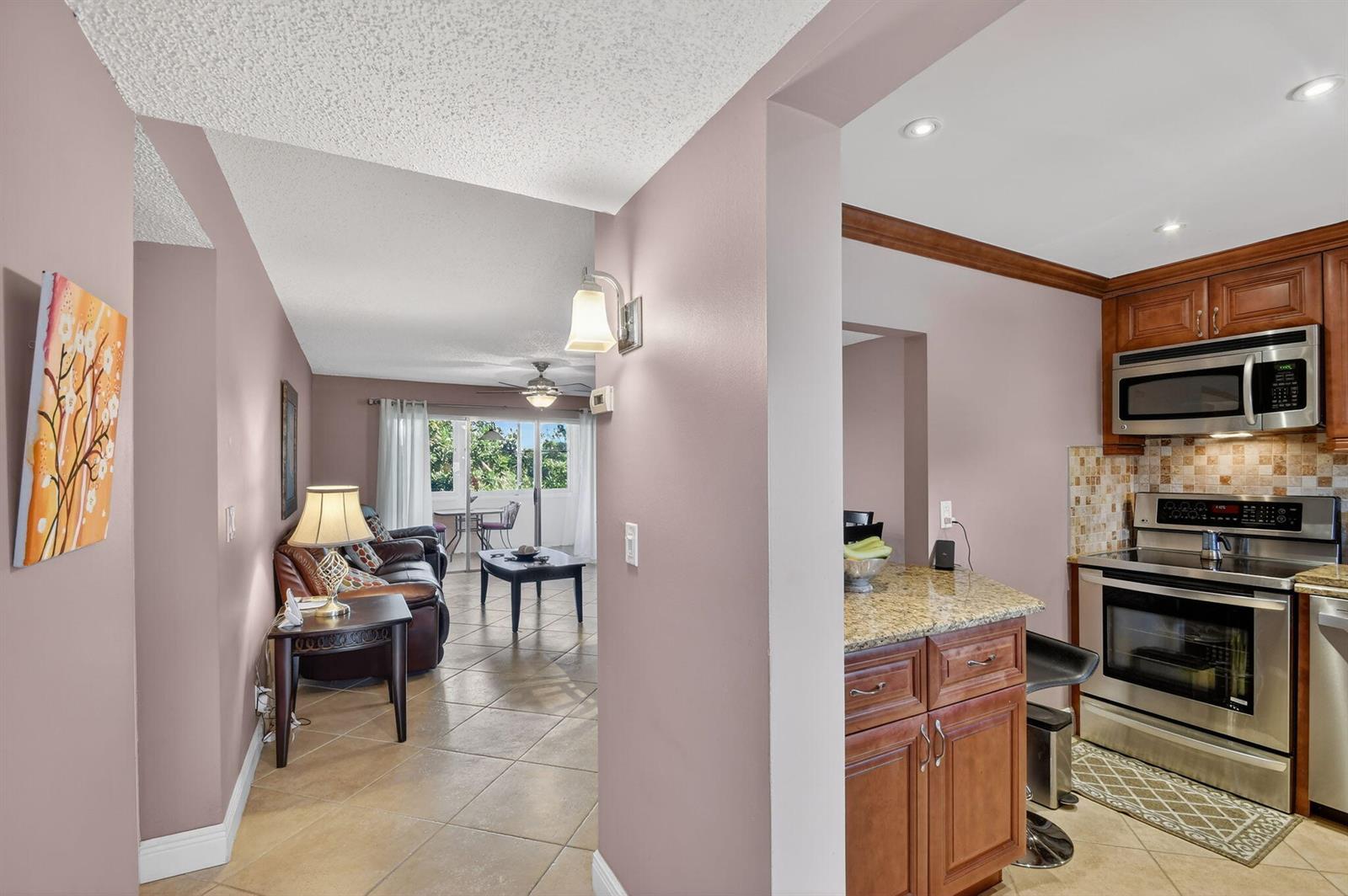 A view from a kitchen with granite countertops looking into a living room with tile floors — 729 Lori Drive # 302, Palm Springs FL 33461, PALM SPRINGS, FL