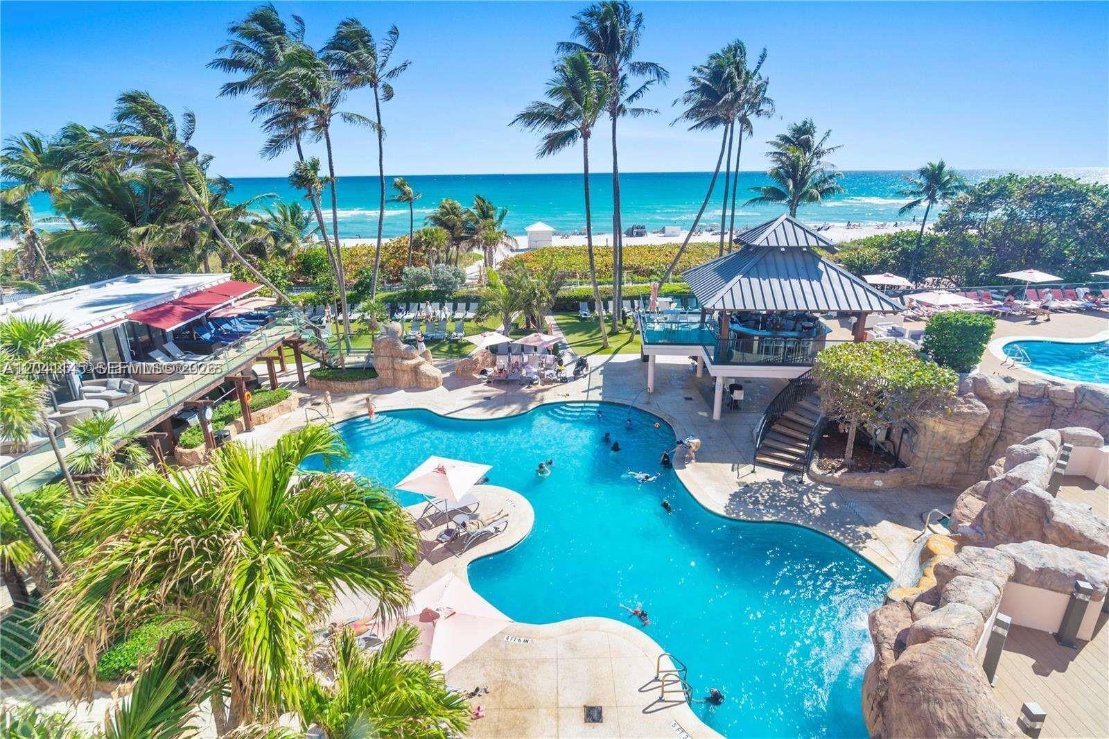 An aerial view shows a resort-style swimming pool with a gazebo, rock features, and beach access — 5225 Collins Ave # 914, Miami Beach FL 33140, MIAMI BEACH, FL