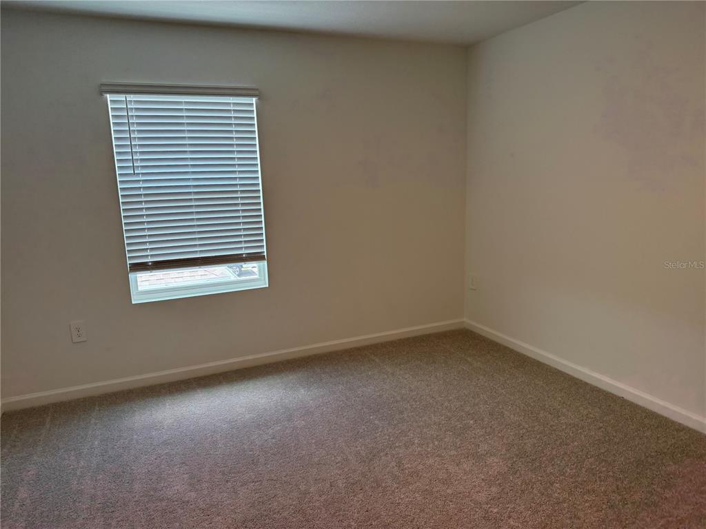 An empty bedroom features beige carpet, off-white walls, and a window with white blinds — 1885 FULFILLMENT DRIVE, KISSIMMEE, FL