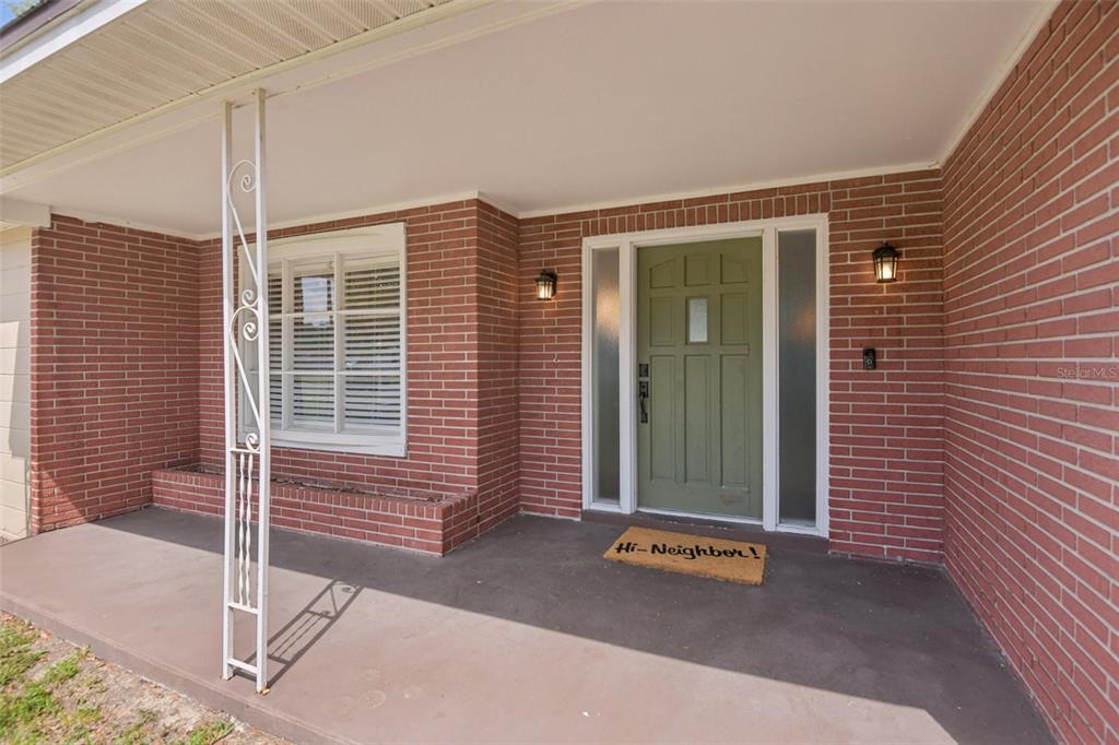 A red brick house exterior features a covered porch, a green front door, and windows — 5942 13TH STREET, ZEPHYRHILLS, FL