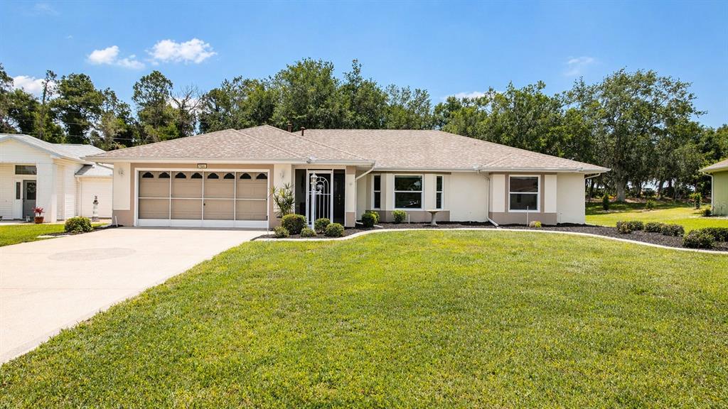 A single-story house with a beige exterior, a multi-car garage, and a large front lawn — 5277 INDIAN OCEAN LOOP, TAVARES, FL