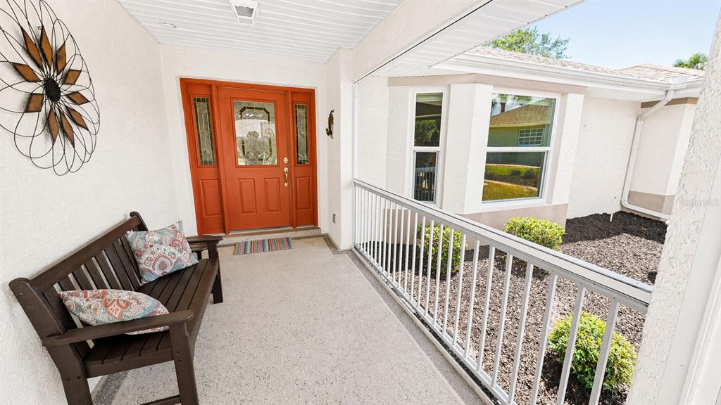 A covered porch features a dark wooden bench, a bright orange door, and white railings — 5277 INDIAN OCEAN LOOP, TAVARES, FL