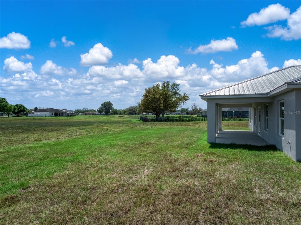 A view of a grassy backyard and a covered patio attached to a house — 7000 WOODMONT COURT, SEBRING, FL