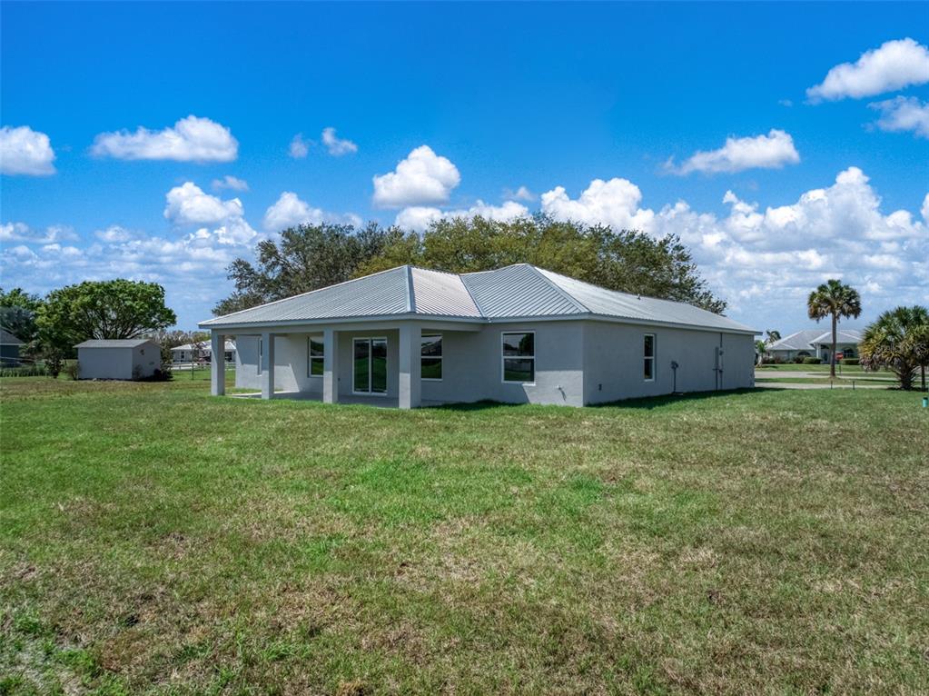 A single-story house with a metal roof and a covered patio sits on a lawn — 7000 WOODMONT COURT, SEBRING, FL