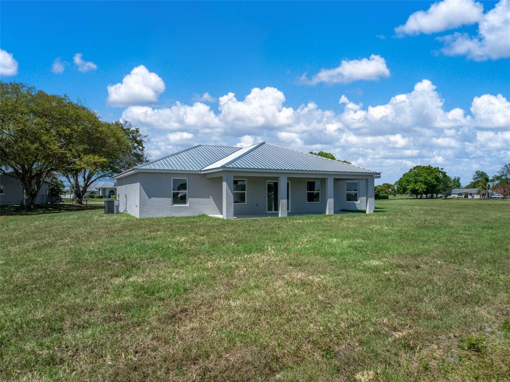 The rear exterior of a single-story house features a covered patio and a metal roof — 7000 WOODMONT COURT, SEBRING, FL